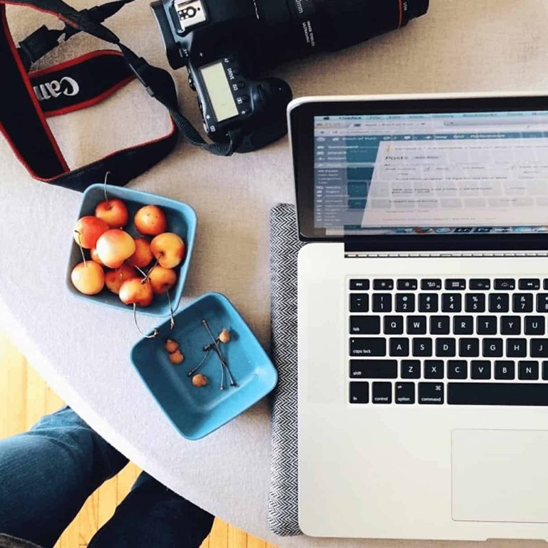 A laptop sitting on a table with fresh cherries.