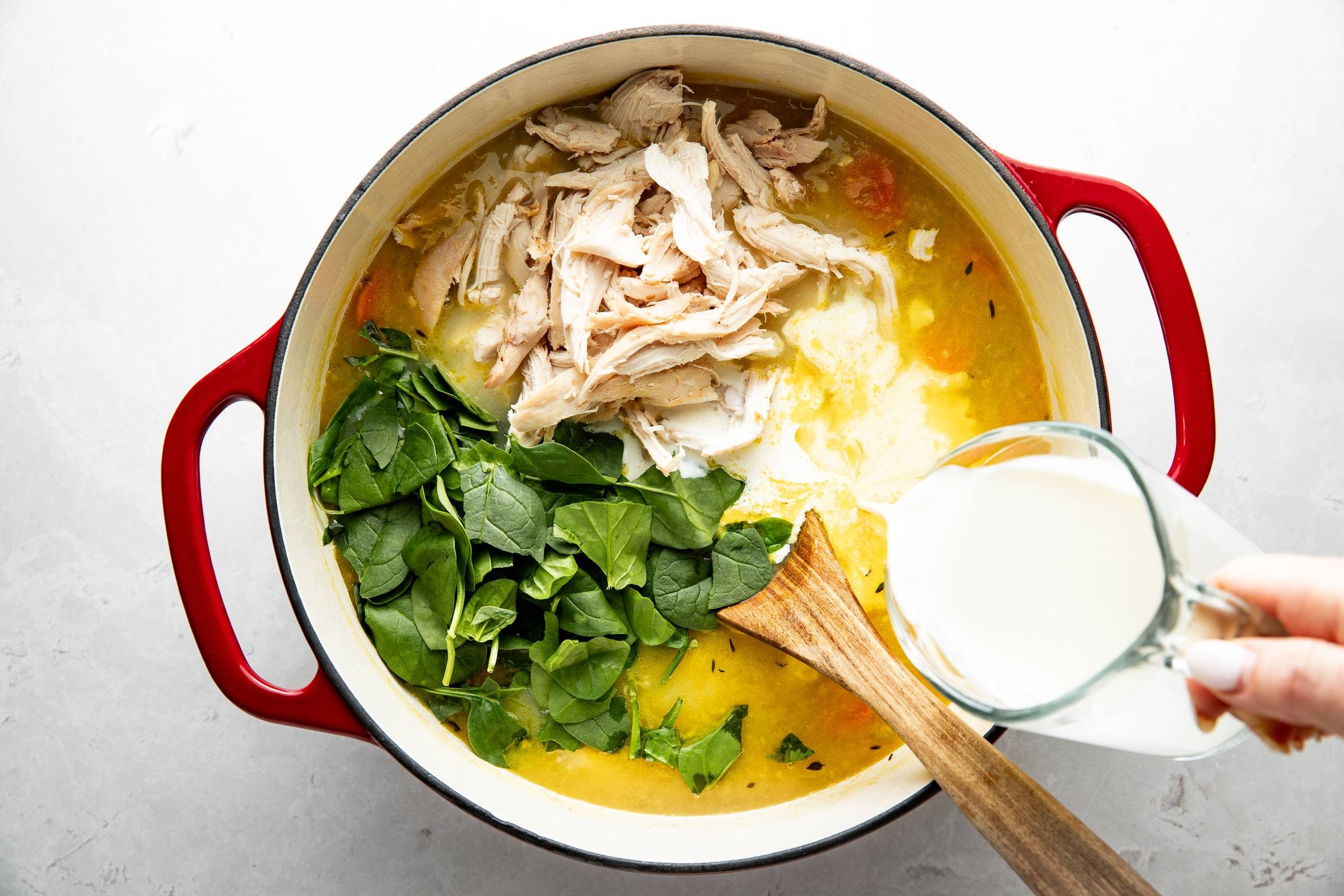 Adding spinach, chicken, and cream to chicken soup.