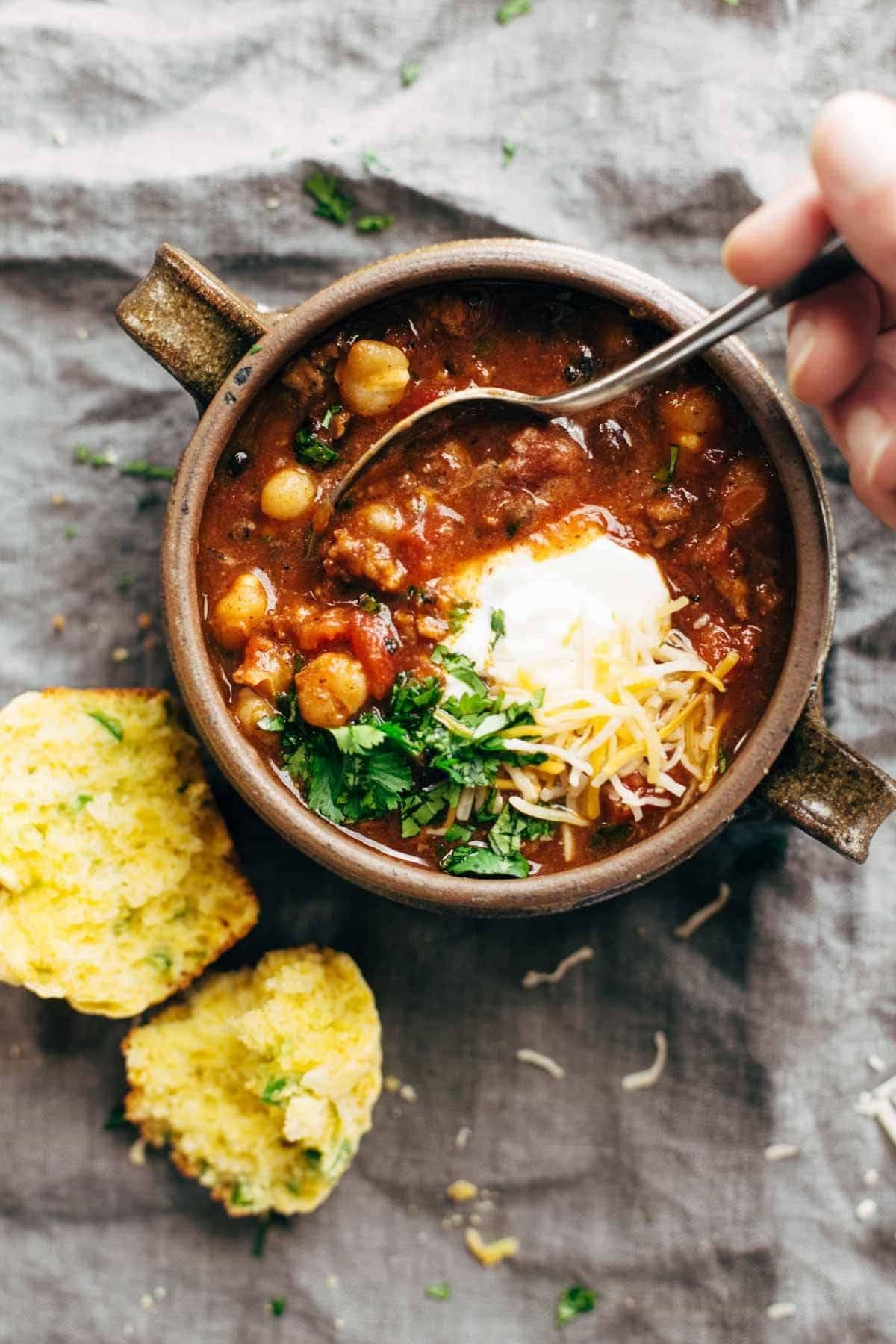 Spicy Posole in a bowl with a spoon and with Cheesy Jalapeño Cornbread Muffins.
