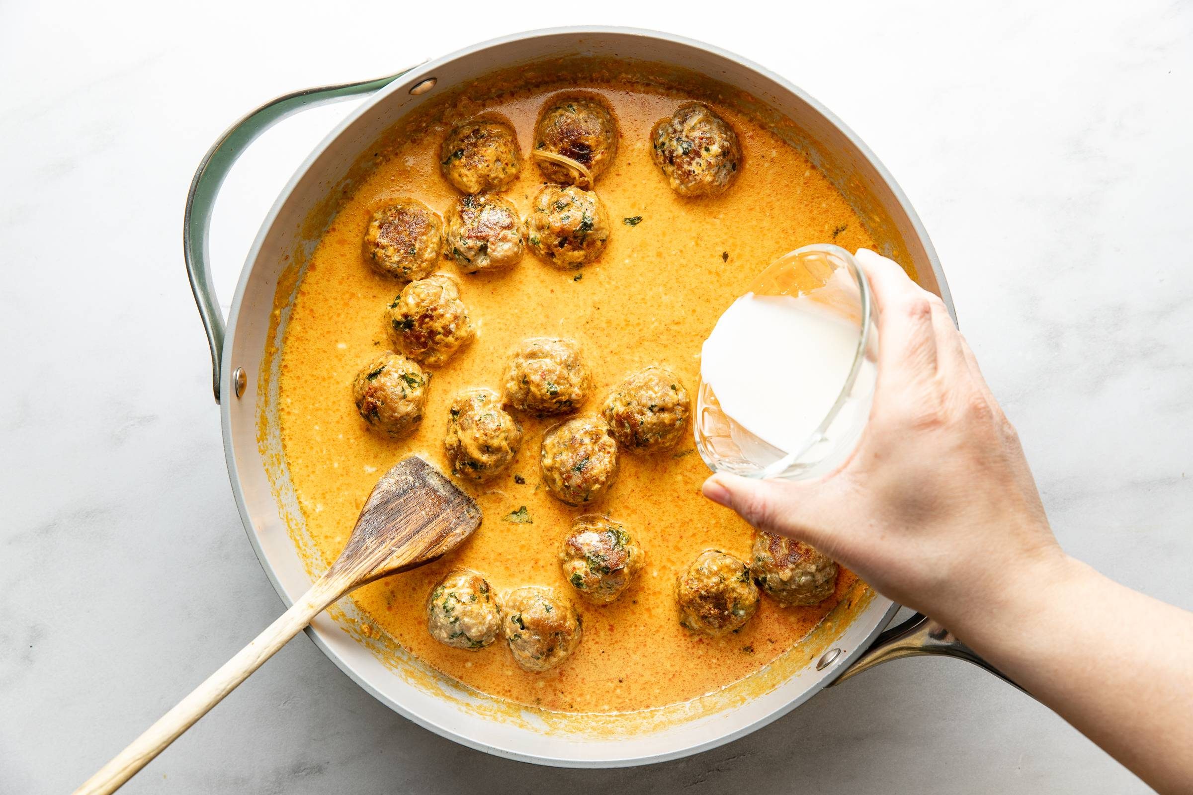 Adding coconut milk to meatballs.