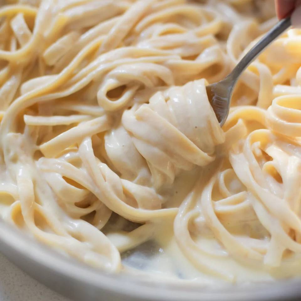 Fettuccine alfredo being twirled with a fork.