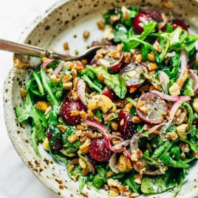 Arugula Salad with grapes, cashews, and pickled red onions in a bowl with a fork.