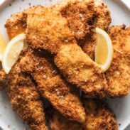Crispy chicken cutlets on a plate with lemon wedges.