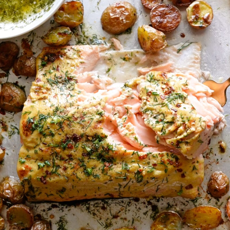Salmon and potatoes on a sheet pan covered in dill.