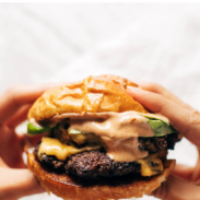 Hands holding a juicy smash burger with sauce.