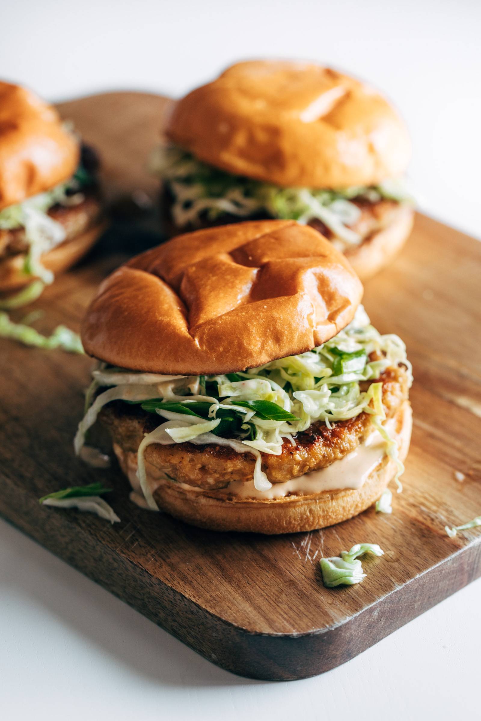 Three chicken teriyaki burgers on a wooden cutting board.