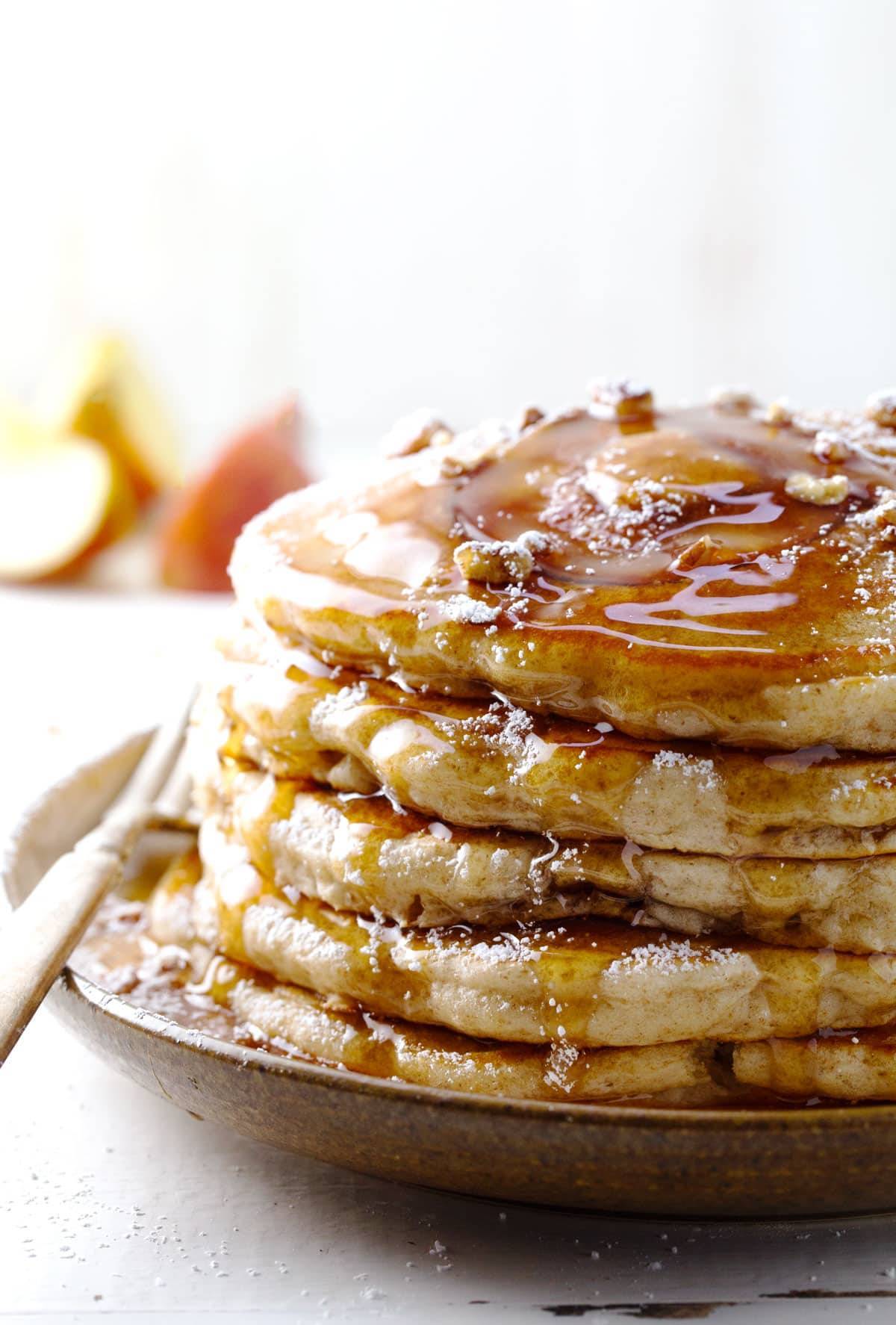 Apple pancakes stacked on a plate with maple syrup.
