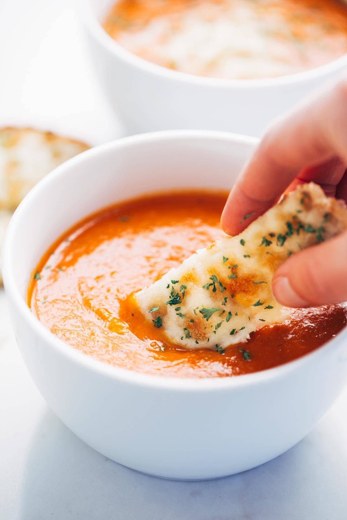 Simple Homemade Tomato Soup with carrots, onions, garlic, tomatoes, broth, and bacon for deliciously rich flavor. Extremely easy to make! | pinchfoyum.com Homemade tomato soup in a bowl with bread dipped in.